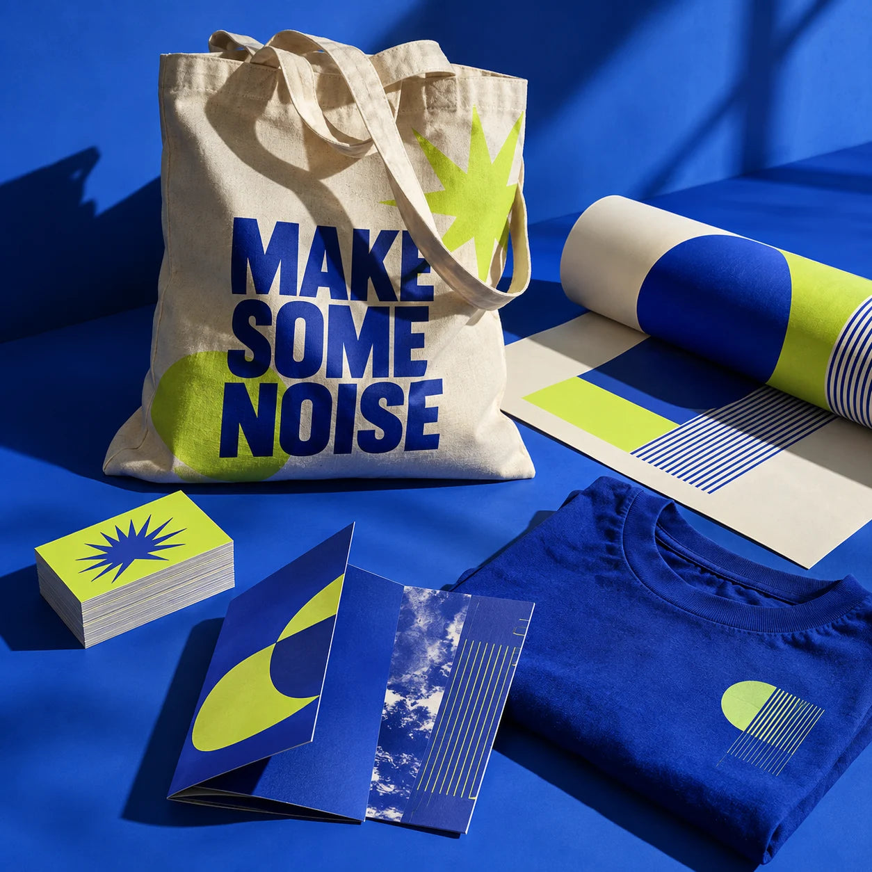 Blue and lime printed business cards, clothing, a tote bag, leaflets and a poster arranged together